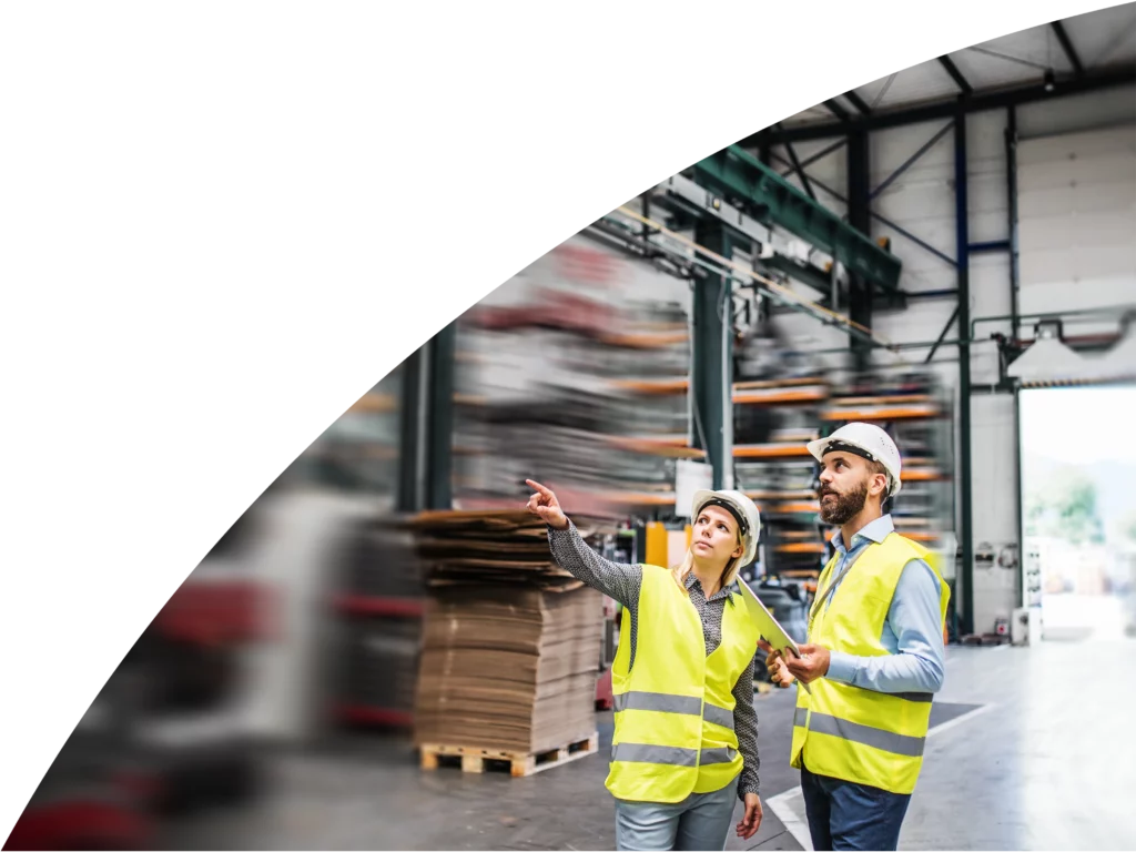 Two workers in a warehouse looking over and evaluating their compliance with regulatory and contractual obligations.